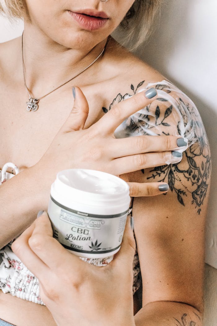 services-04 Tattooed woman applying CBD lotion on shoulder for skincare and relaxation.